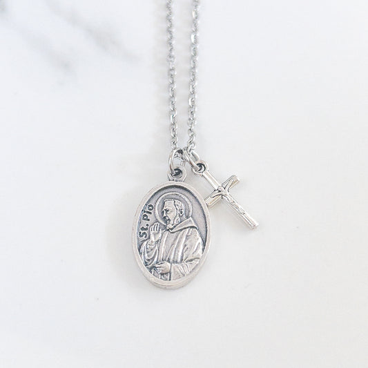 Padre Pio necklace with saint medal and crucifix charm on stainless steel chain, displayed on soft fabric background – Catholic Confirmation gift for men or women.