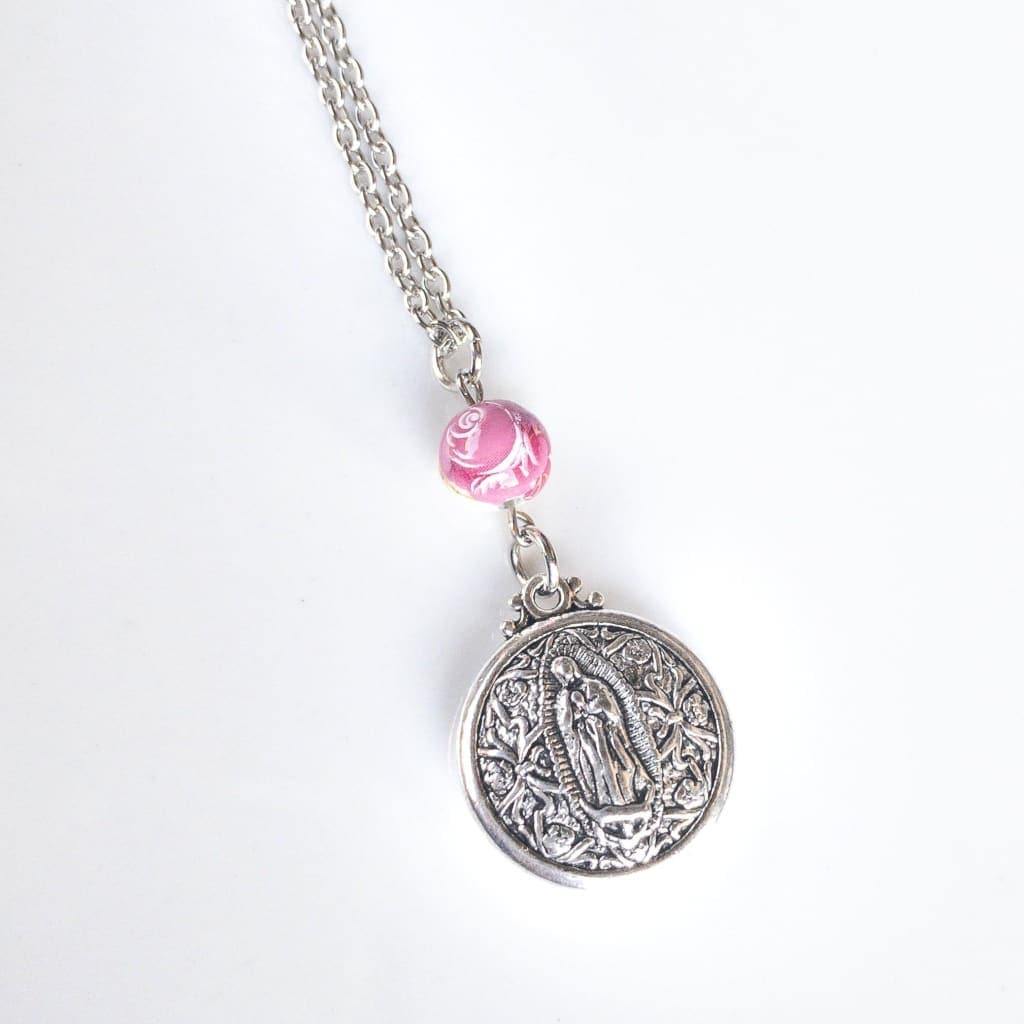 Double Sided Our Lady of Guadalupe Layering Necklace - Sagely Sparrow - Necklace is shown at an angle on a white background with bottom of silver colored chain, pink rose bead, and silver colored circular Our Lady of Guadalupe pendant showing.