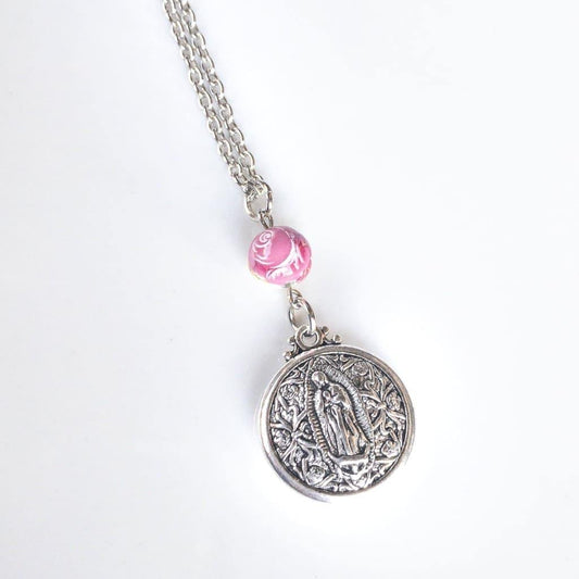 Double Sided Our Lady of Guadalupe Layering Necklace - Sagely Sparrow - Necklace is shown at an angle on a white background with bottom of silver colored chain, pink rose bead, and silver colored circular Our Lady of Guadalupe pendant showing.