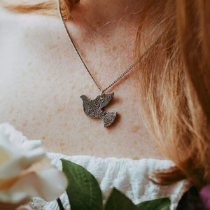 Sagely Sparrow dove necklace modeled on a woman with white top holding flowers