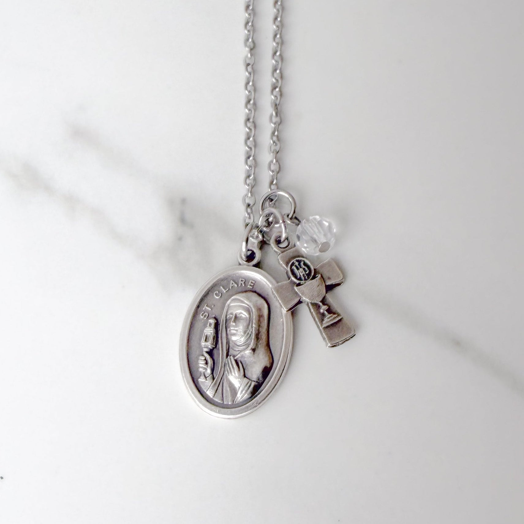 St. Clare of Assisi necklace with oval saint medal, silver-tone chalice and Eucharistic host IHS charm, and clear glass bead on stainless steel chain – Catholic Confirmation gift for girls.