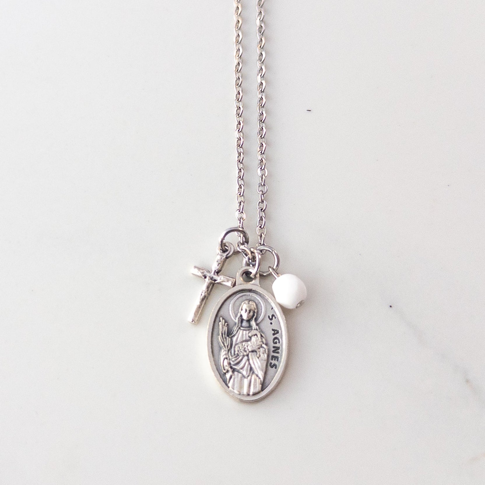 St. Agnes necklace with Italian medal, crucifix charm, and white bead on stainless steel chain, displayed on soft neutral background – Catholic jewelry for girls.