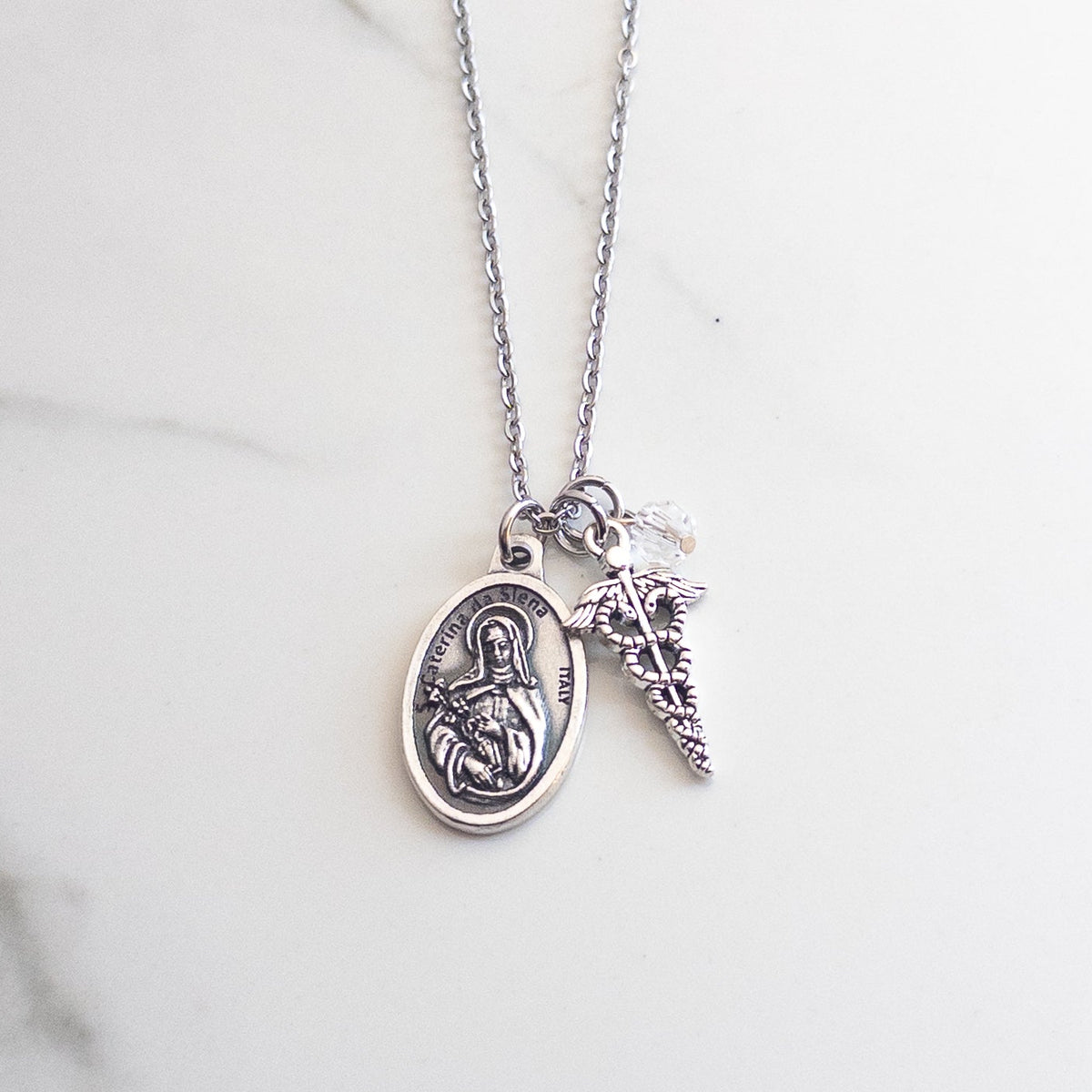 Catholic nurse necklace featuring St. Catherine of Siena medal, silver caduceus charm, and clear glass crystal accent bead.