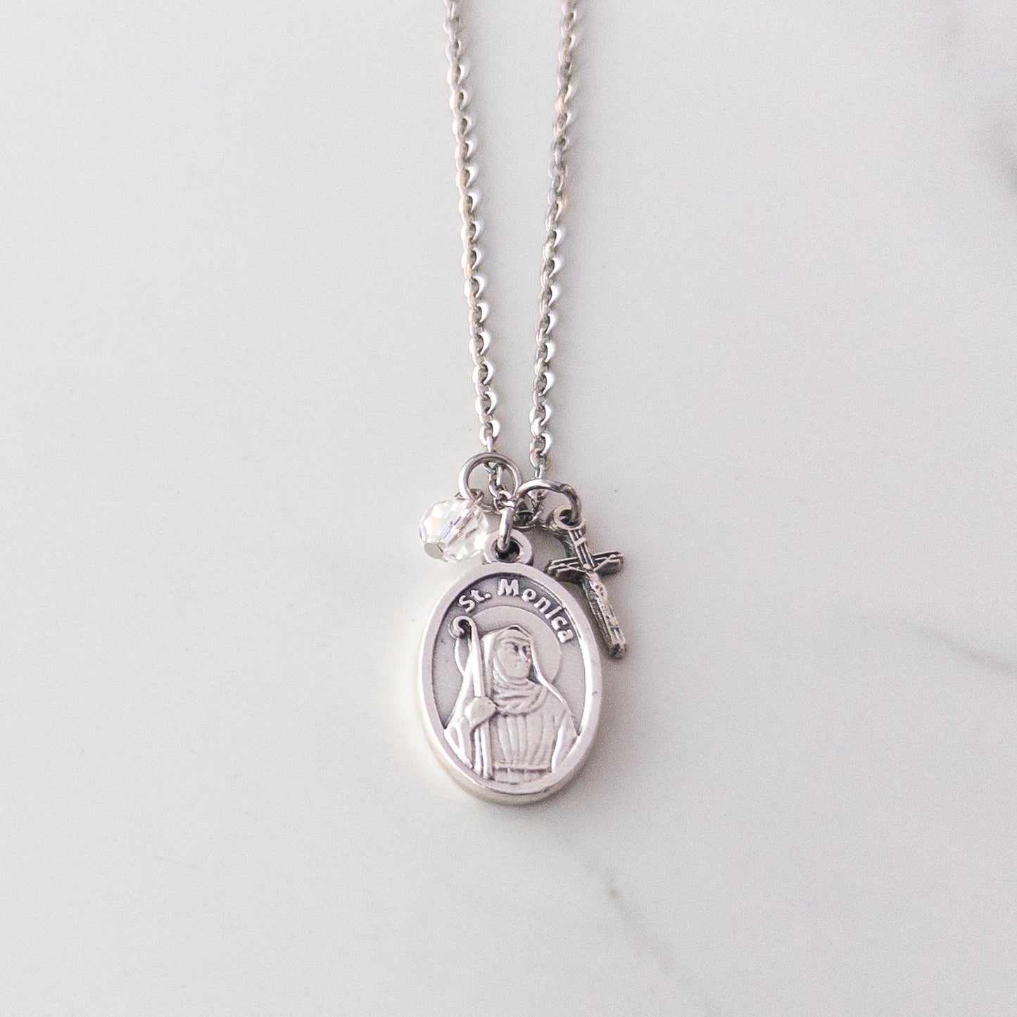 St. Monica and crucifix necklace with clear glass bead on stainless steel chain, displayed on neutral background – Catholic jewelry gift for mothers or Confirmation