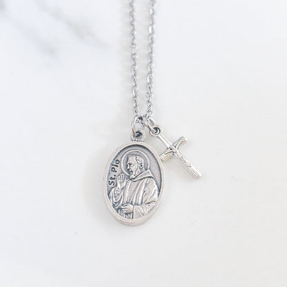 Padre Pio necklace with saint medal and crucifix charm on stainless steel chain, displayed on soft fabric background – Catholic Confirmation gift for men or women.