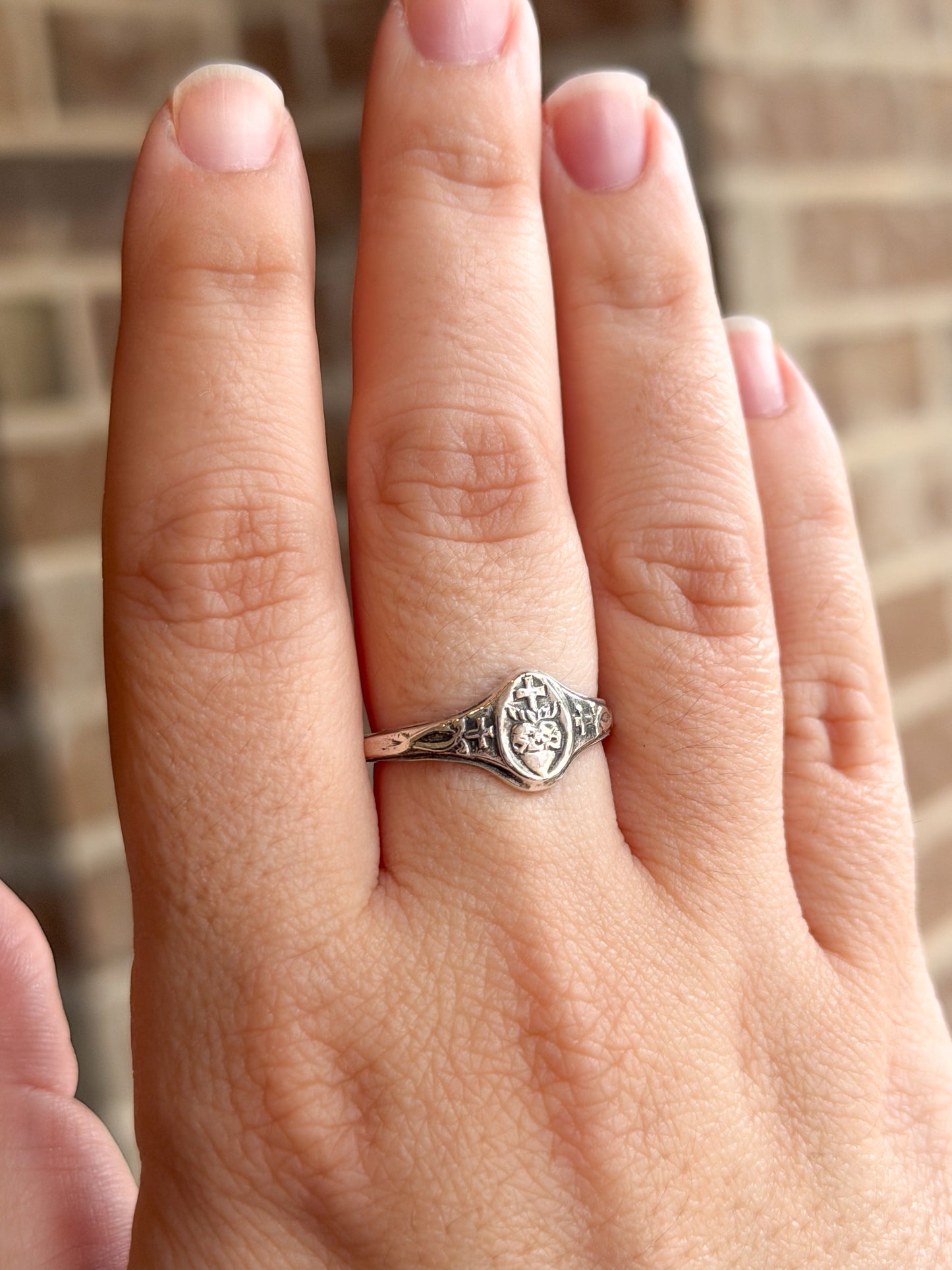 Silver Sacred Heart ring on a person's finger with a blurred background