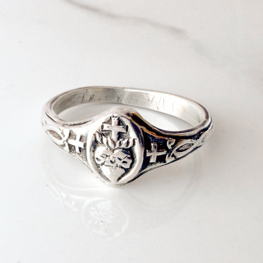 Sterling silver Sacred Heart ring with vintage-style detailing, displayed on neutral tile background — handmade Catholic jewelry for women.