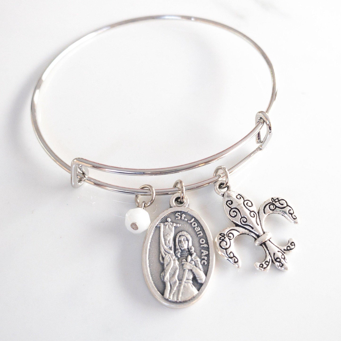 St Joan of Arc bangle bracelet with silver saint medal, fleur de lis charm, and white faceted glass bead on adjustable silver slider bracelet.