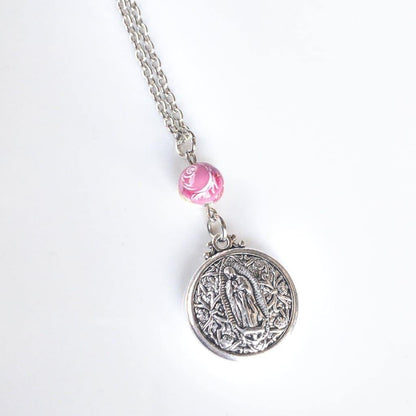 Double Sided Our Lady of Guadalupe Layering Necklace - Sagely Sparrow - Necklace is shown at an angle on a white background with bottom of silver colored chain, pink rose bead, and silver colored circular Our Lady of Guadalupe pendant showing. 